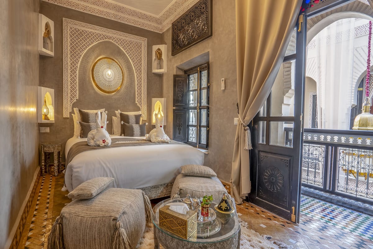 A luxurious bedroom with a large bed, ornate wall decorations, and a balcony with a view.