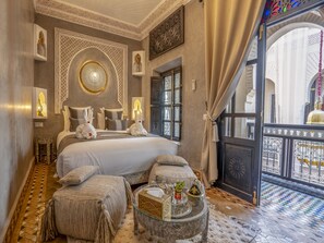 A luxurious bedroom with a large bed, ornate wall decorations, and a balcony with a view.