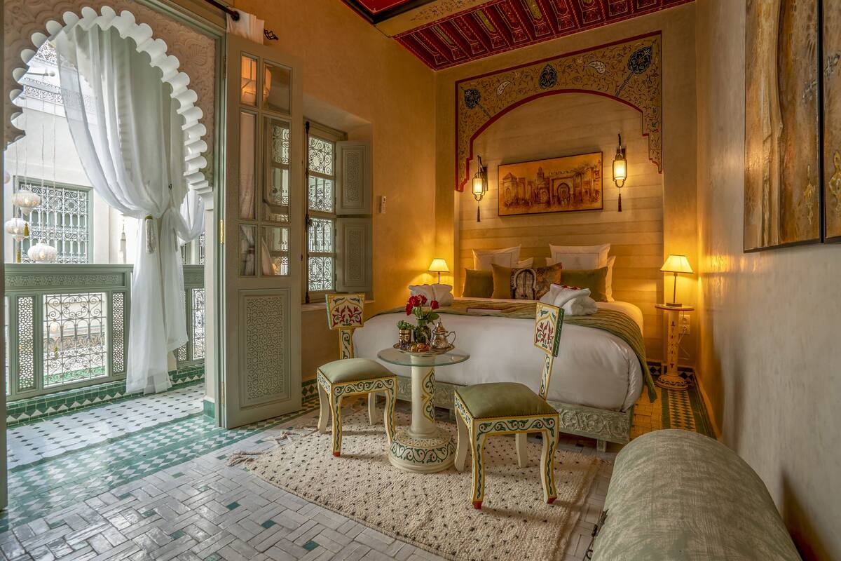 A traditional Moroccan room with a bed, two chairs, a small table, and a decorative wall.