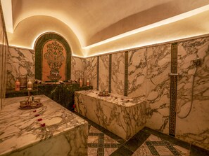 A luxurious bathroom with marble walls, a central marble sink, and a shower with a decorative shower head.