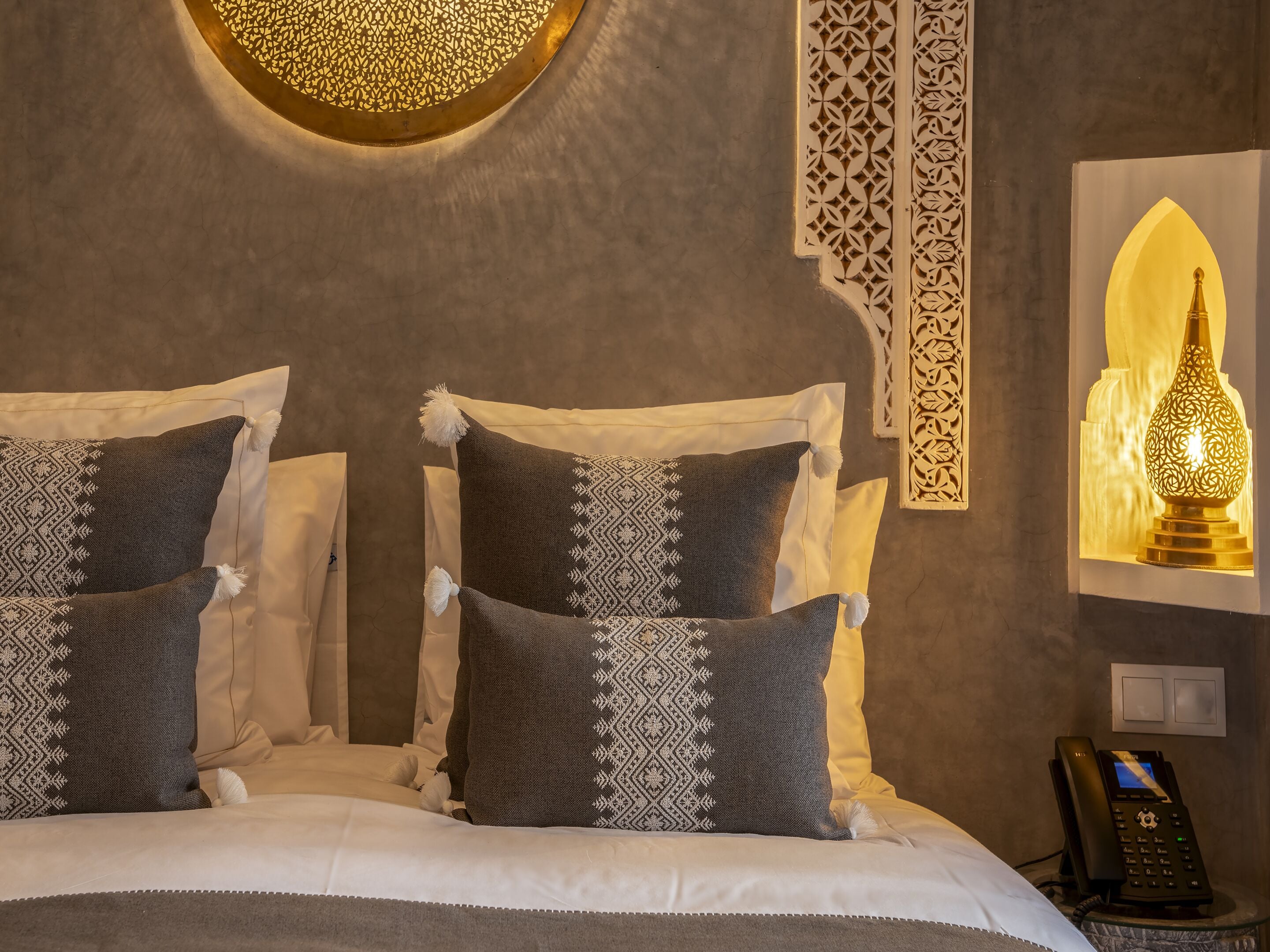 A bed with two pillows, a wall-mounted phone, and a decorative wall light.