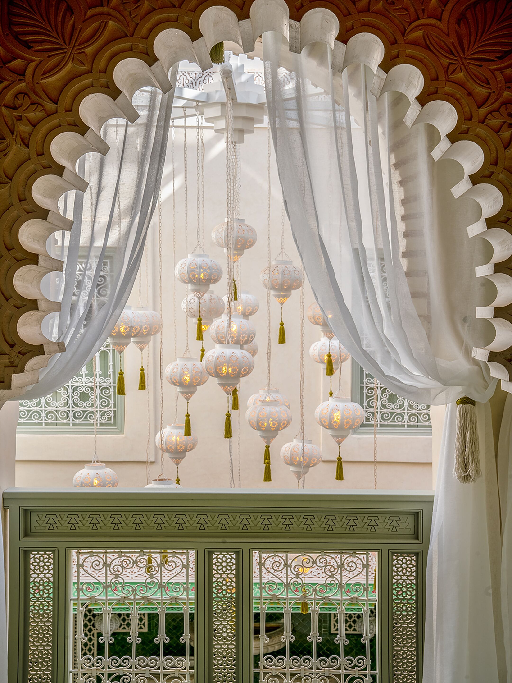 Een kamer met decoratieve witte gordijnen, hangende lantaarns en gedetailleerde raamroosters.
