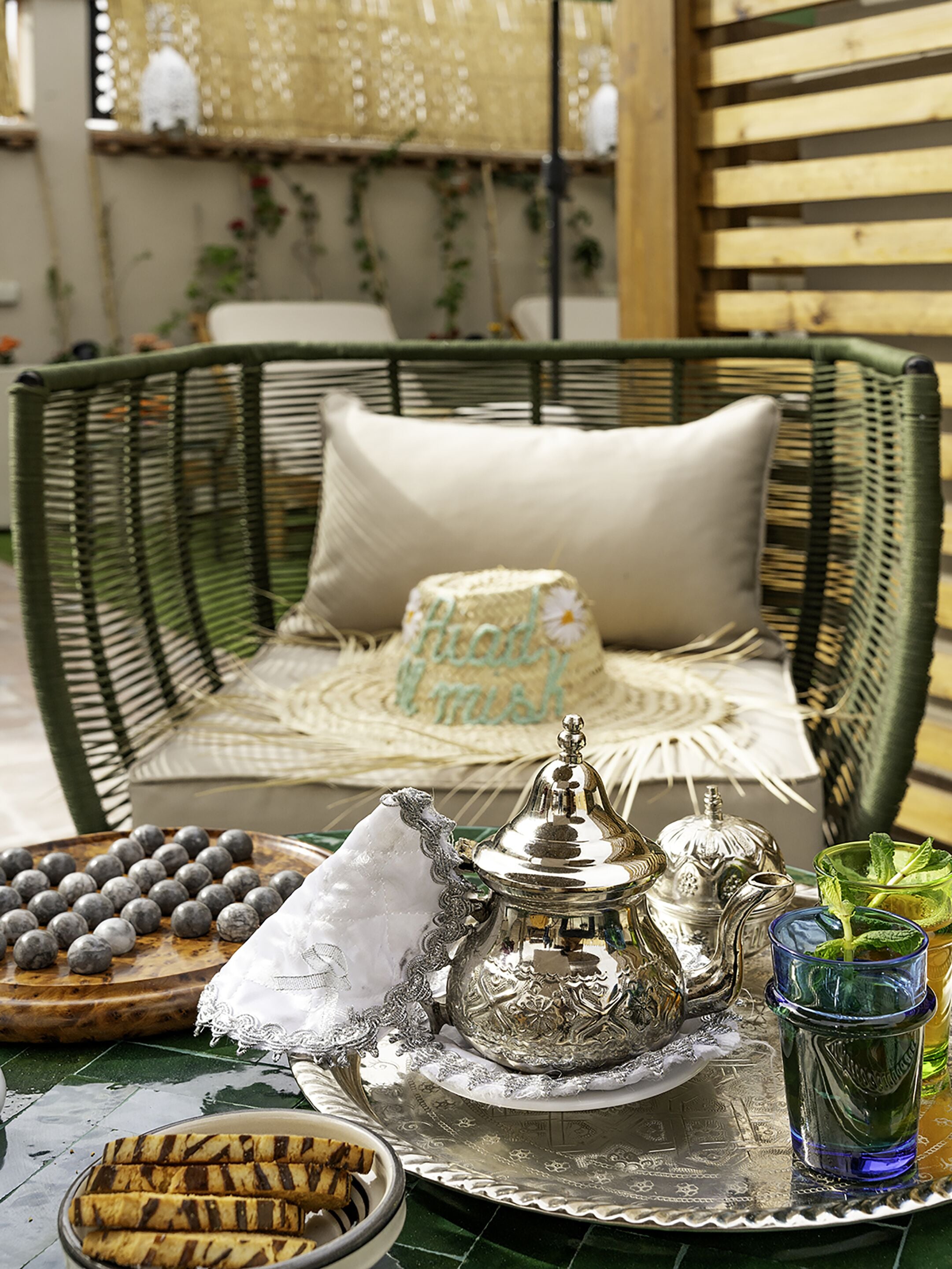 A wicker chair with a cushion, a tray with silverware, a plate of cookies, and a glass of water.