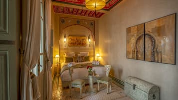 Una habitación tradicional marroquí con una cama, dos mesitas de noche, una pequeña mesa y un cofre decorativo.