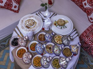A table set with various dishes and utensils, surrounded by decorative pillows and a vase with a red rose.