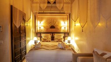 A well-lit bedroom with a large bed, two bedside lamps, and a decorative wall piece above the bed.