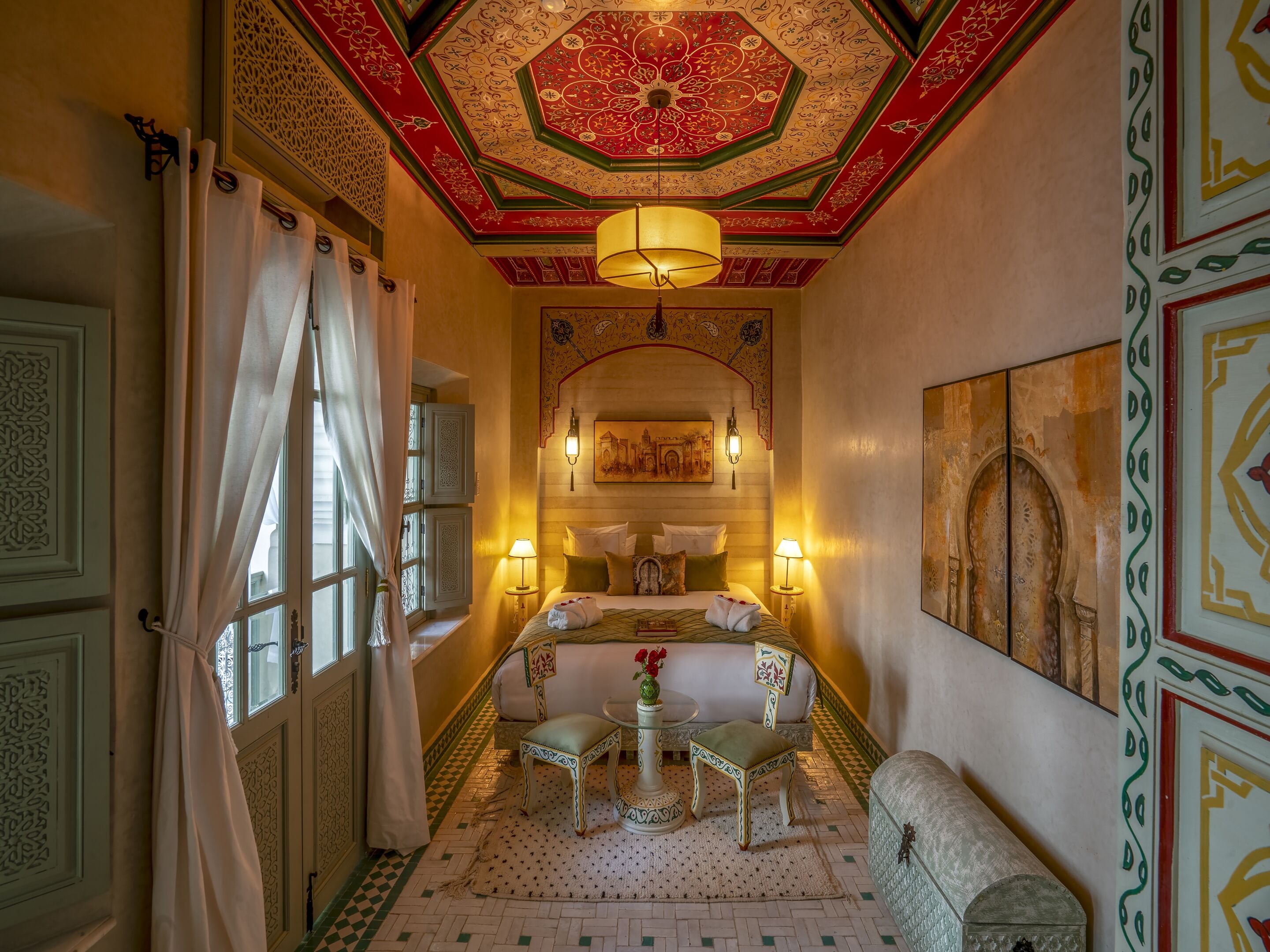 A traditional room with a bed, two side tables, a bench, and a decorative ceiling.