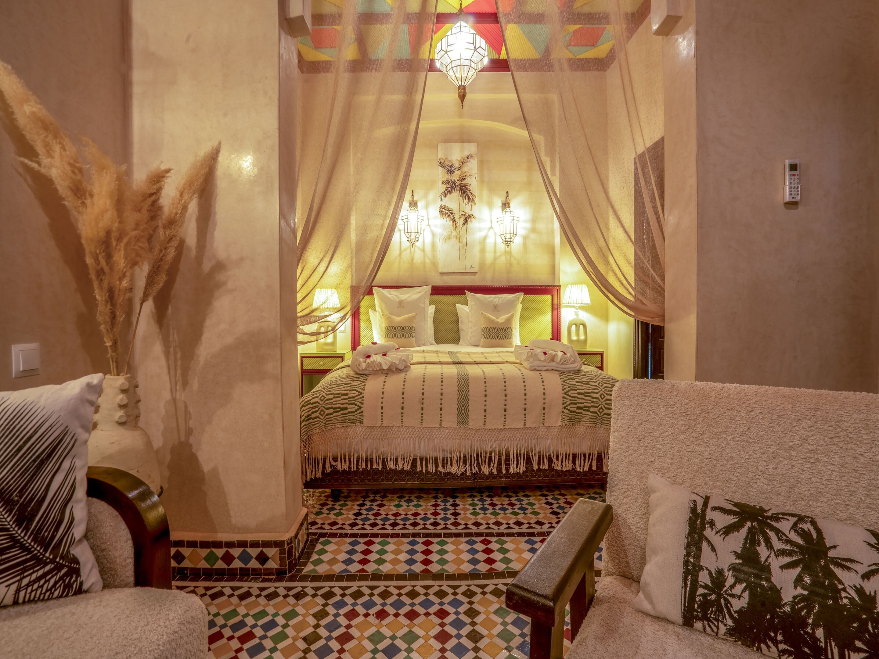 A hotel room with a bed, a chair, a nightstand, a lamp, a wall-mounted phone, and a decorative wall piece.
