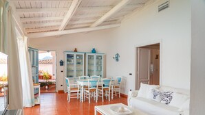 Uma sala espaçosa com um sofá branco, uma mesa de jantar com cadeiras e uma cozinha com armários.
