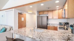 A modern kitchen with granite countertops, stainless steel appliances, and wooden cabinetry. - Beachfront luxury | Walk to dining & shops (Kihei)
