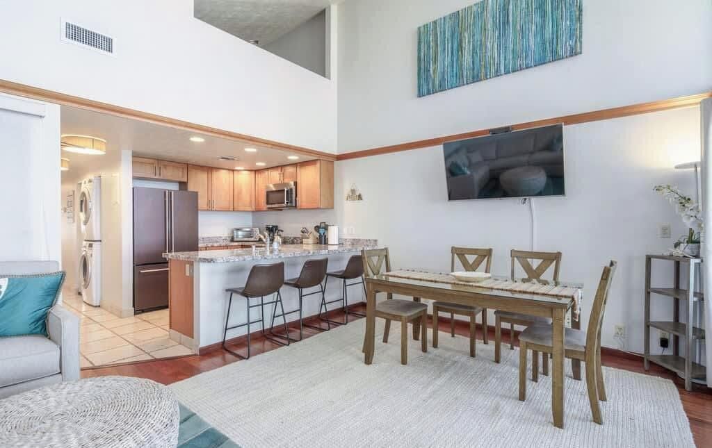 A modern kitchen with a central island, bar stools, and a dining table with chairs.