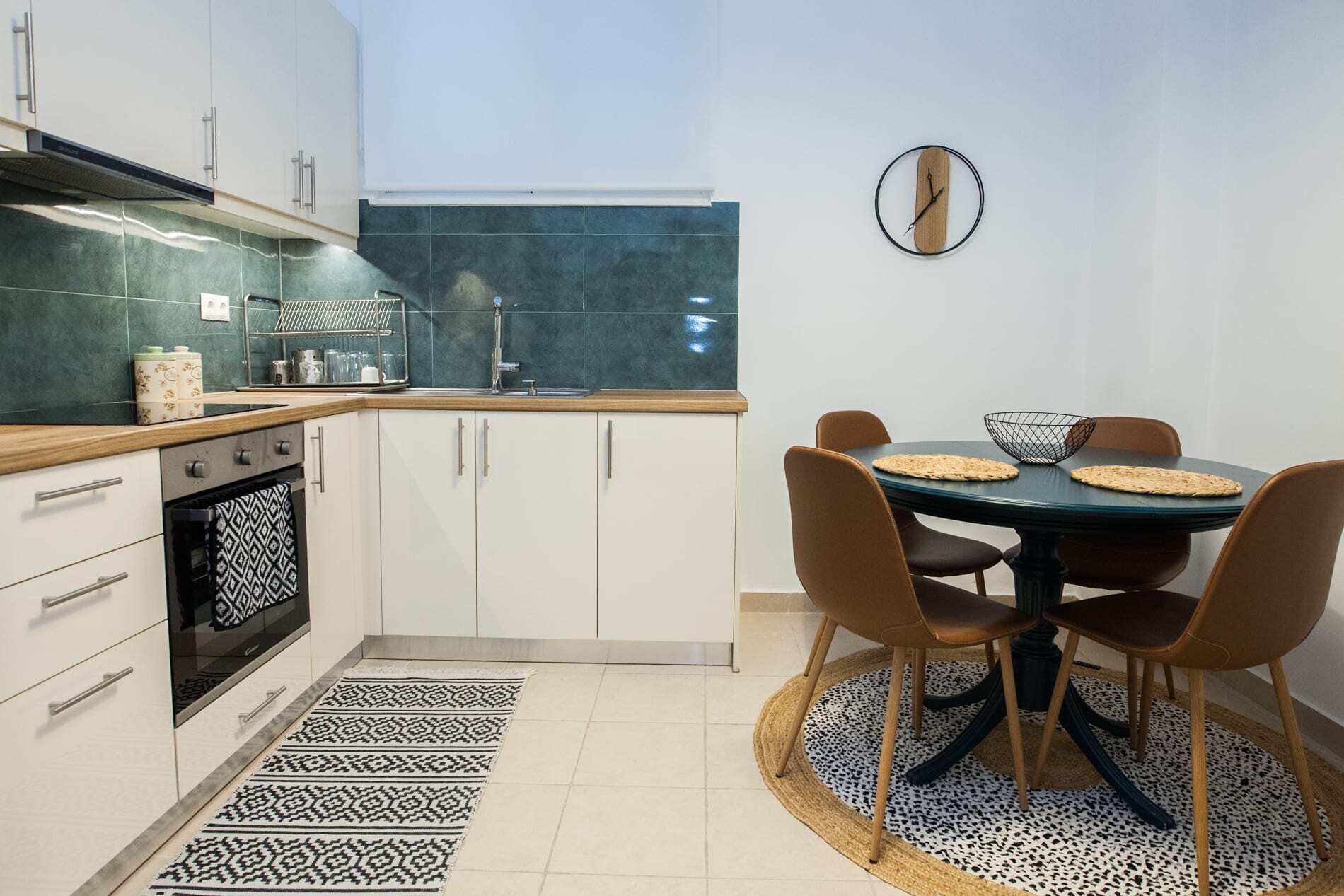 Une cuisine moderne avec des armoires blanches, un four encastré et un coin repas comprenant une table ronde et des chaises marron.