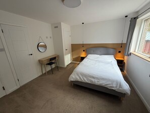 A bedroom with a bed, a desk, a chair, a bedside table, a lamp, a mirror, and a window. -  Cairngorms National Park apartment in Carrbridge (Carrbridge)