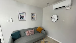 A modern living room with a grey sofa, two framed pictures, a round mirror, and a patterned rug.