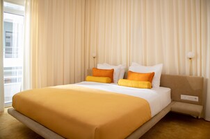 Quarto de hotel com uma cama grande, uma mesa de cabeceira e uma janela com cortinas.