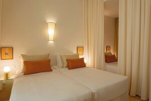 A double bed with white and orange bedding, a wall-mounted light, and framed pictures on the wall.