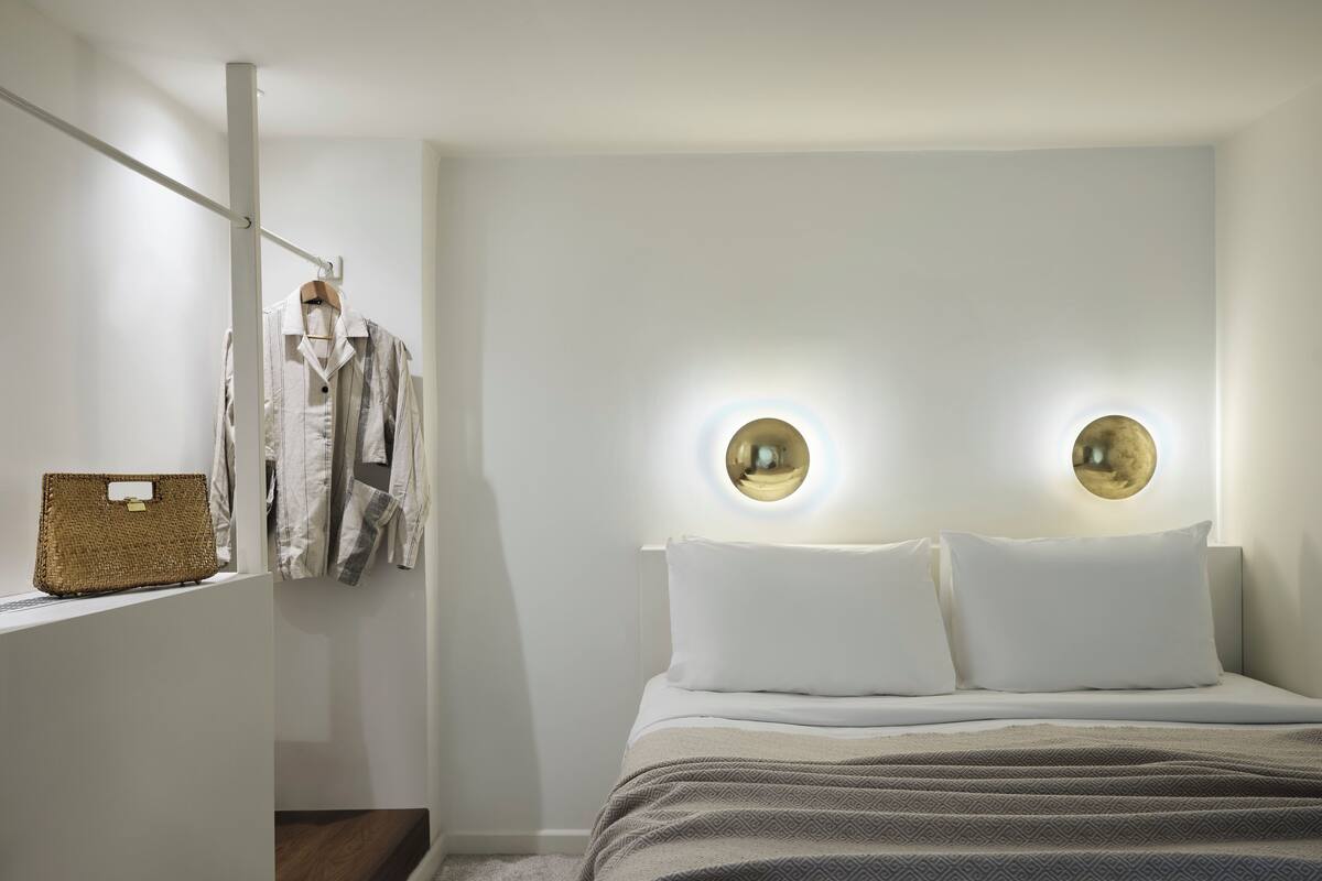 A bedroom with a bed, two wall-mounted circular lights, a hanging basket, and a coat rack.