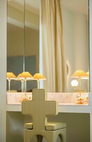A room with a mirror, a chair, and three lamps on a table.
