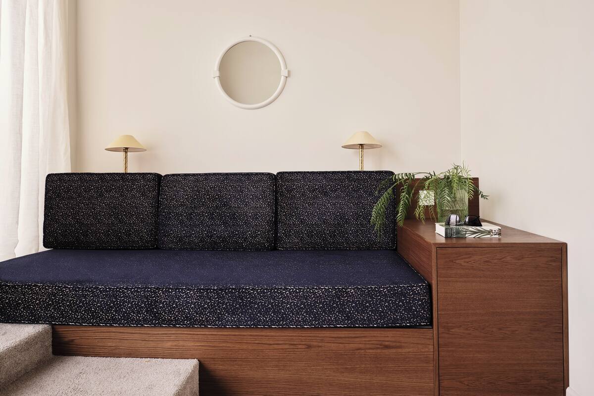 A modern living room with a dark speckled sofa, two floor lamps, a round mirror, and a wooden side table with a plant.