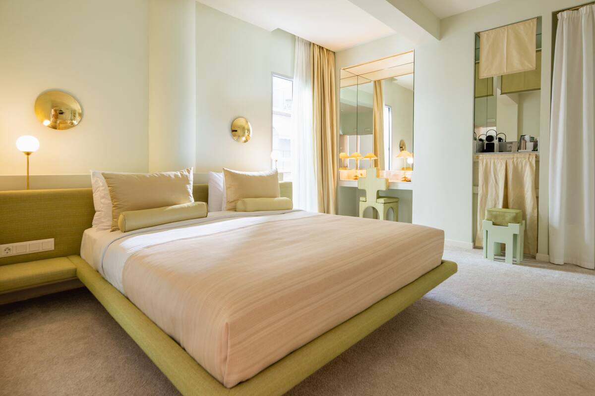 A neatly arranged hotel room with a large bed, a bedside table, a mirror, and a small seating area.