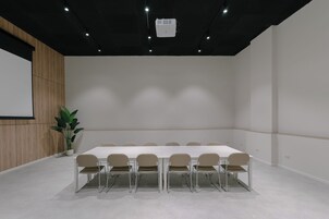 Una sala de conferencias con una larga mesa, seis sillas, una pantalla de proyector y una planta en maceta.