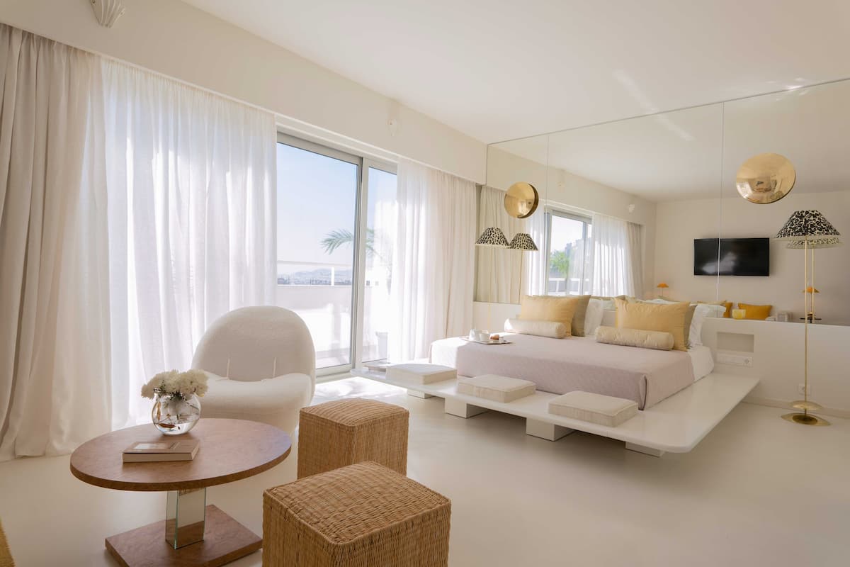 A modern hotel room with a large bed, a seating area with a round table, and a large window with curtains.