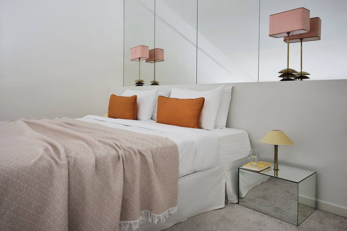 A modern bedroom with a bed, bedside table, lamp, and a mirror.