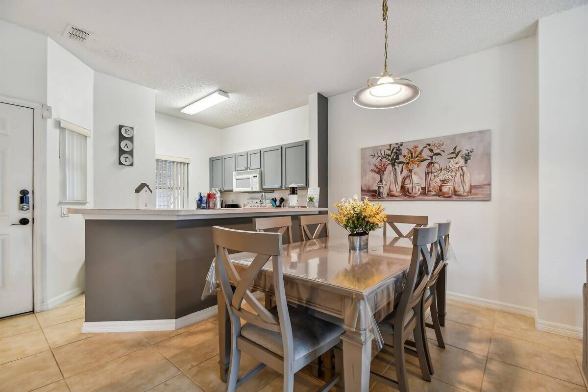 A modern kitchen with grey cabinets, a central island, and a dining area with wooden chairs and a vase of flowers.