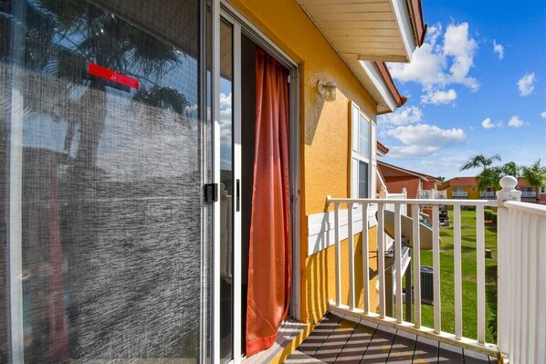 Un balcón con barandilla blanca, puerta de cristal y pared amarilla.