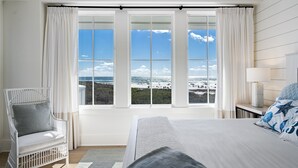 A bedroom with a large window, a bed, a chair, and a nightstand with a lamp. - PANORAMIC GULF FRONT in WATERSOUND BRIDGES! VIEWS, OUTDOOR BALCONY, 30A Area (Watersound)