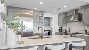 A modern kitchen with a central island, grey cabinetry, stainless steel appliances, and a marble backsplash. - PANORAMIC GULF FRONT in WATERSOUND BRIDGES! VIEWS, OUTDOOR BALCONY, 30A Area (Watersound)