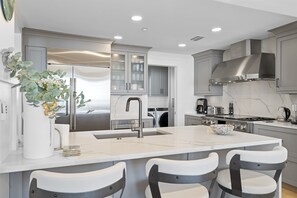 Une cuisine moderne dotée d’un îlot central, de meubles de couleur grise, d’appareils électroménagers en acier inoxydable et d’un dosseret en marbre.