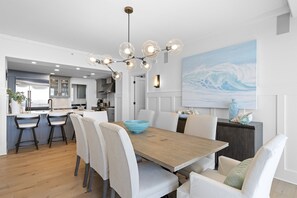 A modern kitchen with a wooden dining table, white chairs, and a blue bowl.