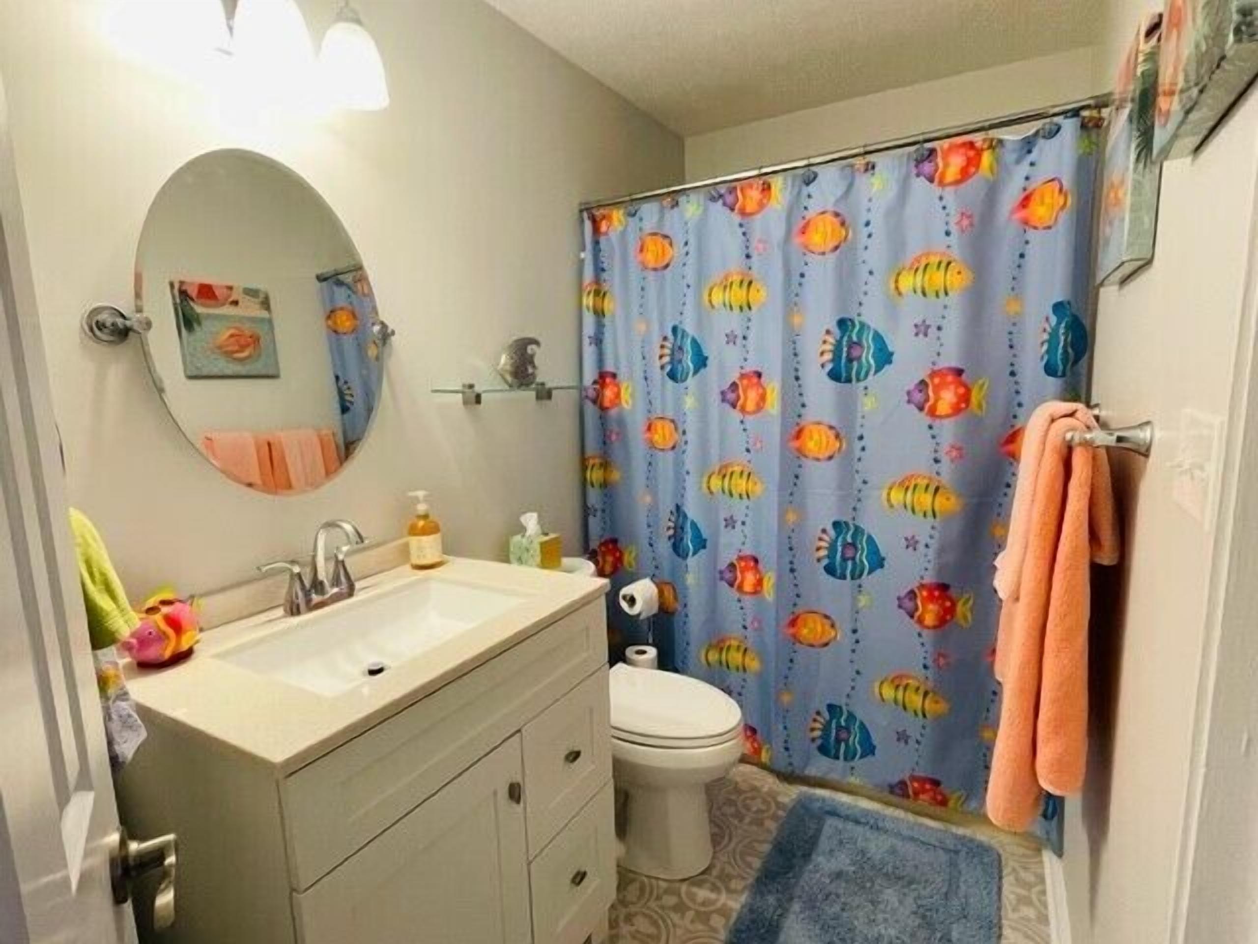 Un baño con lavamanos, espejo, inodoro y cortina de ducha con estampado de peces.