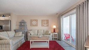 Een woonkamer met gestreepte banken, een salontafel, een rood vloerkleed, een lamp en wanddecoratie met een nautisch thema.