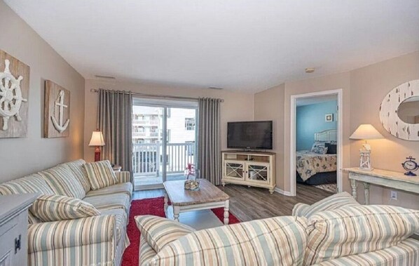 Een gezellige woonkamer met gestreepte banken, een televisie en een balkon met gordijnen.