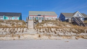 Une propriété située en bord de mer, dotée d’un escalier en bois menant à une terrasse, le tout entouré de dunes de sable.