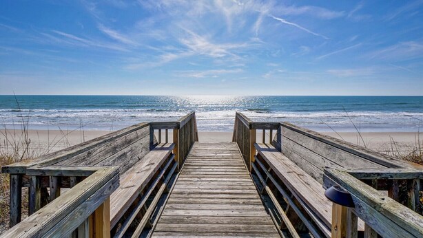 Une promenade en bois menant à une plage, avec un ciel dégagé.
