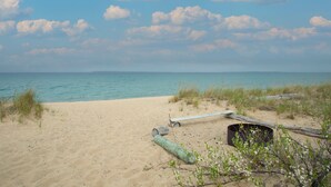 A sandy beach with a wooden bench and a log, surrounded by grass and plants. - Beachfront 2 bedroom condo, Glen Arbor (Glen Arbor)