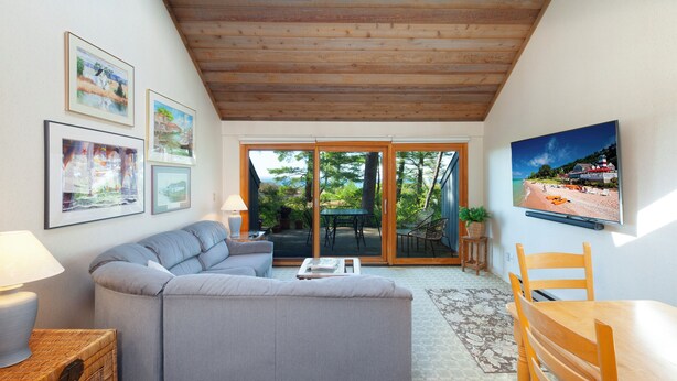A cozy living room with a sofa, a coffee table, and a TV mounted on the wall. There are framed pictures on the wall and a wooden ceiling. - Beachfront 2 bedroom condo, Glen Arbor (Glen Arbor)