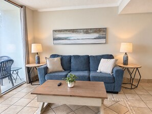 A living room with a blue sofa, two side tables with lamps, a coffee table, and a painting on the wall.