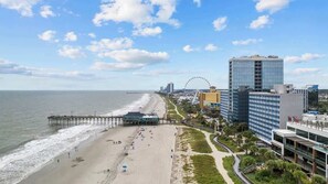 Et bybillede ved stranden med en mole, et pariserhjul og moderne bygninger.