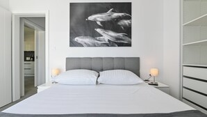 Habitación de hotel moderna con una cama grande, dos lámparas de noche, un cabecero tapizado de color gris y una fotografía en blanco y negro de delfines en la pared.