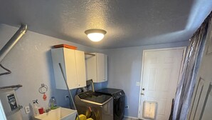 Une petite cuisine équipée d’un évier, d’une cuisinière et d’un four à micro-ondes. Un balai et un seau se trouvent sur le sol.