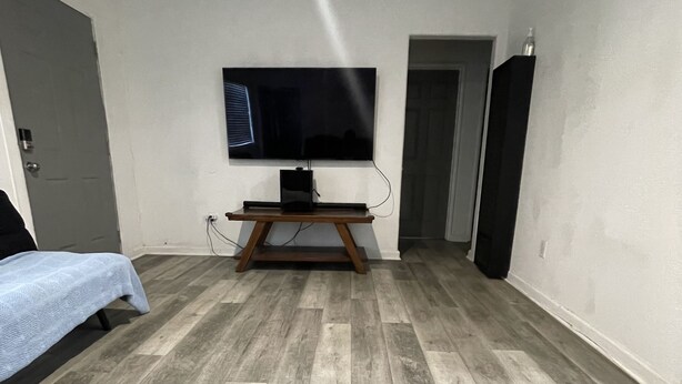 Une pièce dotée d’un téléviseur à écran plat fixé au mur, d’un plancher en bois, d’un lit recouvert d’une courtepointe bleue et d’une porte.