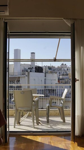 A balcony with two white chairs and a table, overlooking a cityscape with buildings and a clear sky.