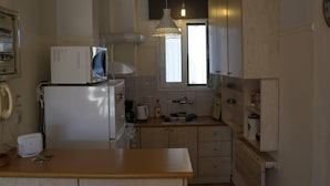 A compact kitchen with a microwave, refrigerator, and a small sink. There is a wooden countertop and a hanging light fixture above the sink. - Immaculate 2-bed Apartment in Zografou (Zografos)