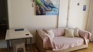 A room with a beige sofa, a small table with a book, and a painting on the wall. - Immaculate 2-bed Apartment in Zografou (Zografos)