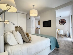 Una habitación de hotel moderna con una cama, un televisor, una zona de comedor con sillas y un reloj de pared.