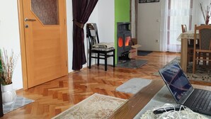 A living room with a wooden door, a fireplace, a dining table with chairs, and a laptop on a table.